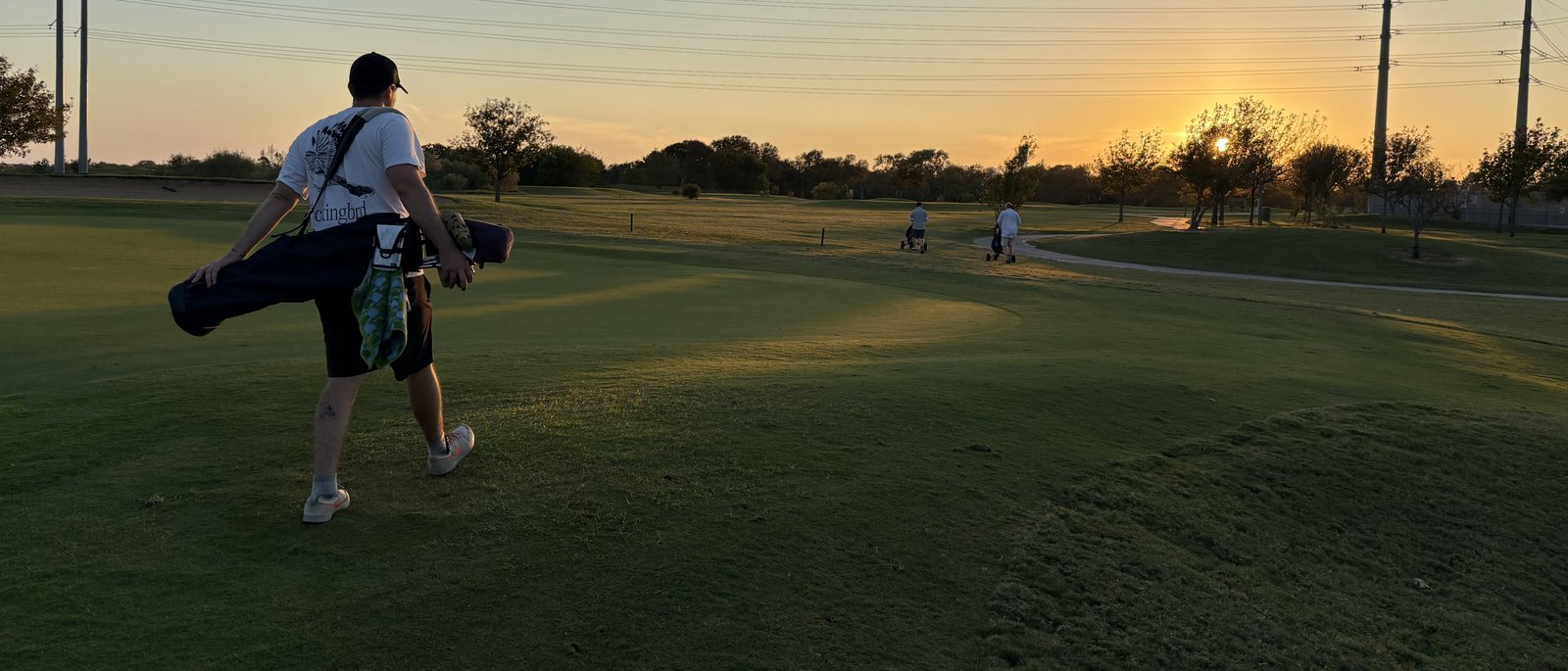 A golfer walking down the fairway at Morris Williams with his carry bag as the sun sets