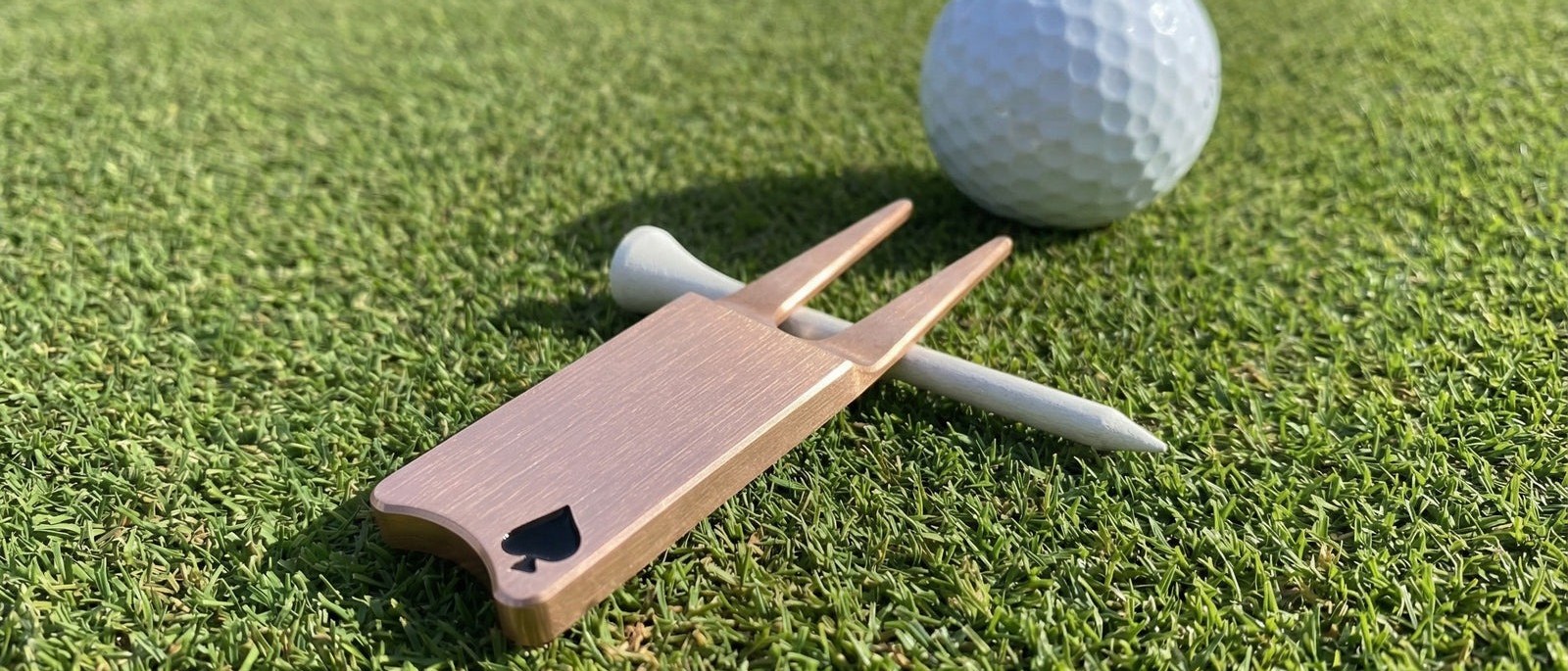 A copper Provision divot tool and a white tee lying on the green beside a golf ball