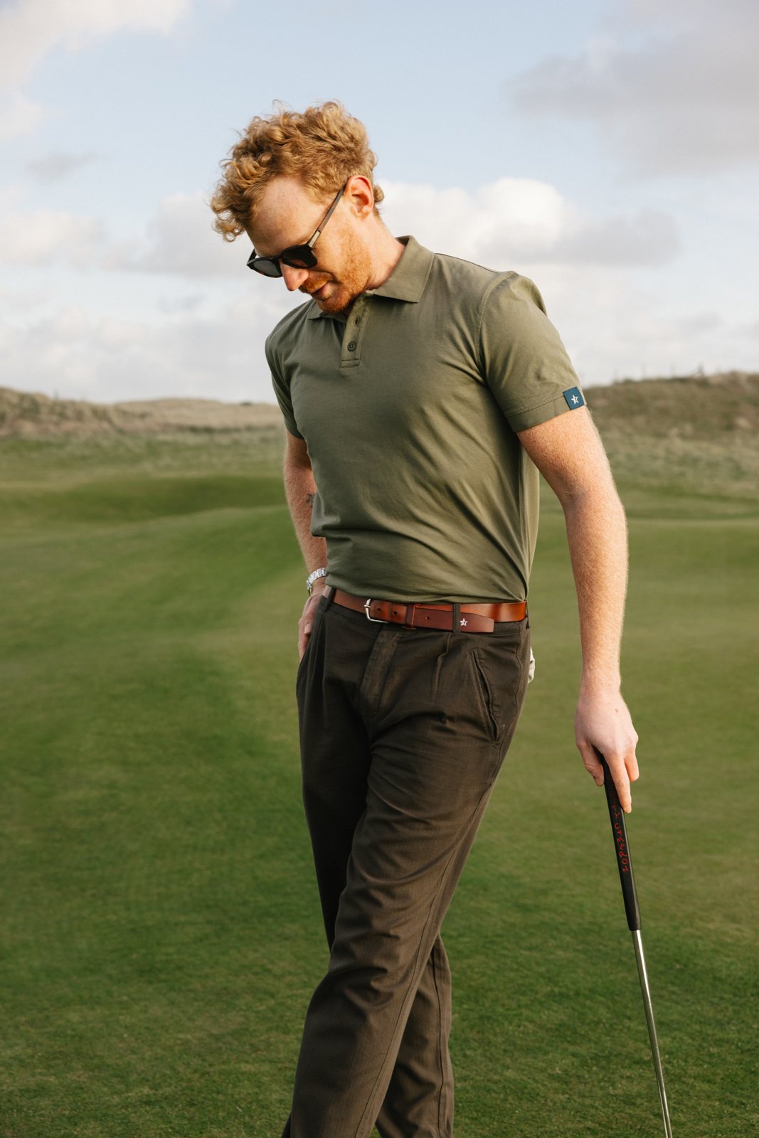 A golfer in an olive Sounder polo and dark trousers on a links course