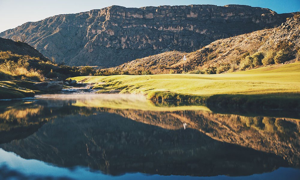 A green reflected in water under desert cliffs at Lajitas