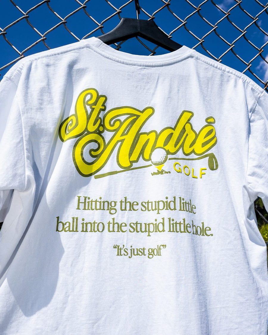 The back of a white St. André tee hung on a chain-link fence