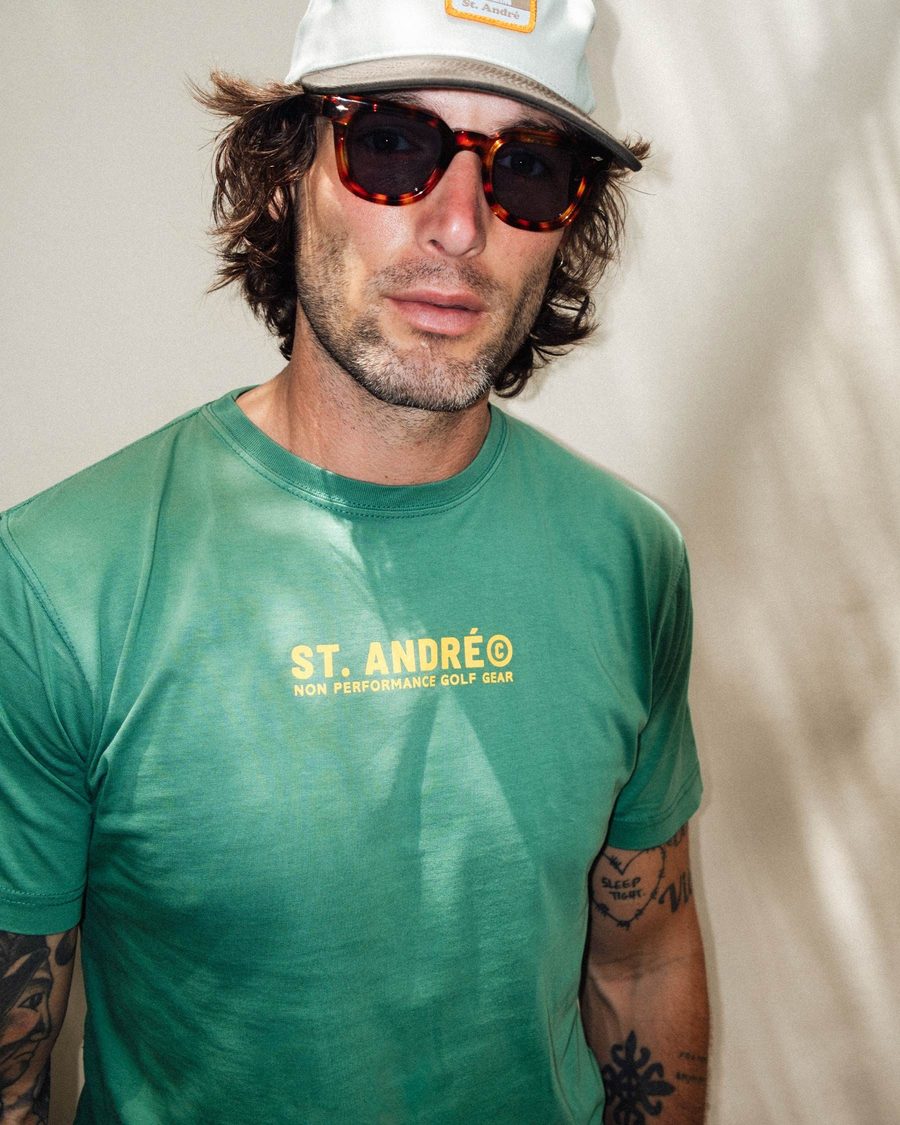 A man in a green St. André tee and a white cap with sunglasses