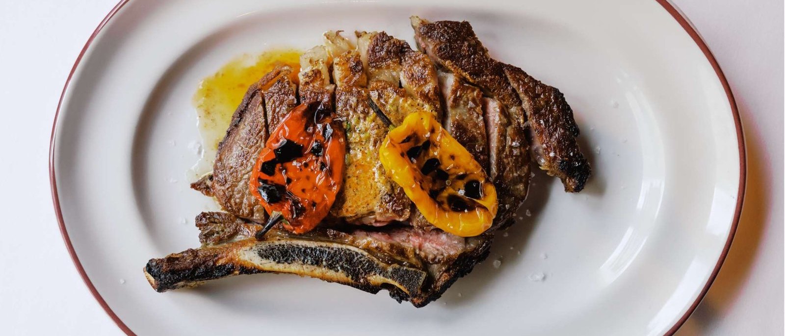 A sliced dry-aged bone-in ribeye with charred peppers on an oval plate at The Driskill Grill