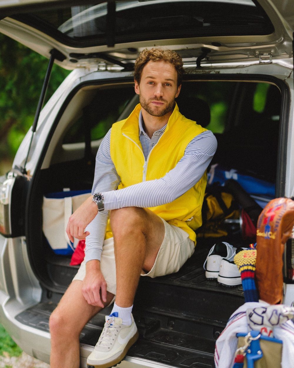 A man in a yellow Tech Vest sitting in the back of a car full of golf gear