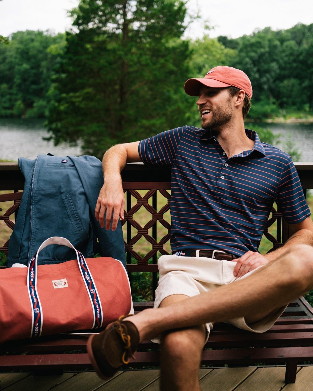 A man in a navy striped polo sitting on a dock bench with a duffel bag