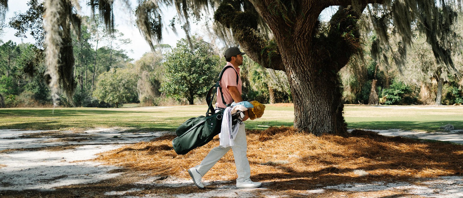 A golfer walking under live oaks carrying a Sun Mountain stand bag