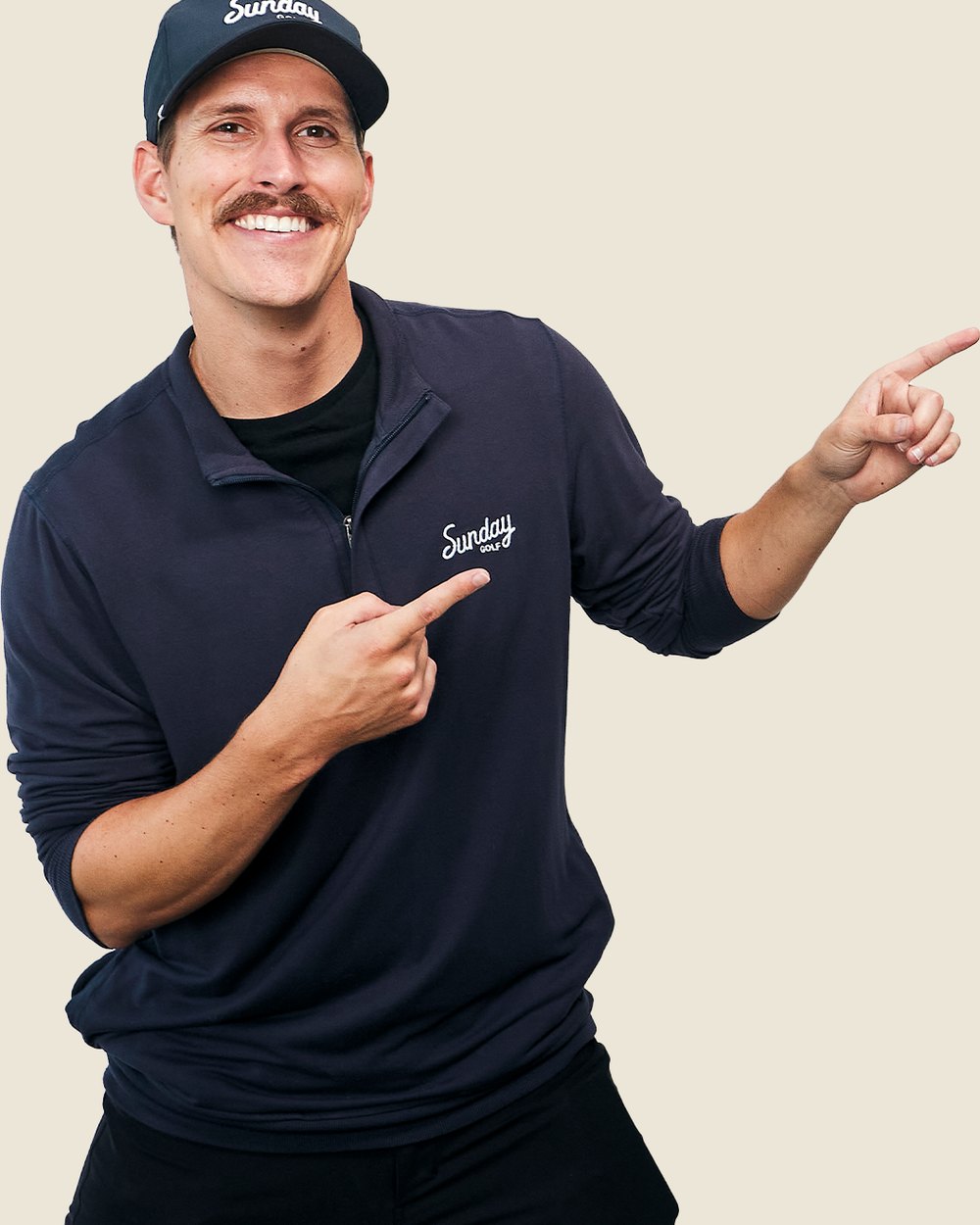 A man with a mustache in a navy Sunday Golf quarter-zip pointing at the logo