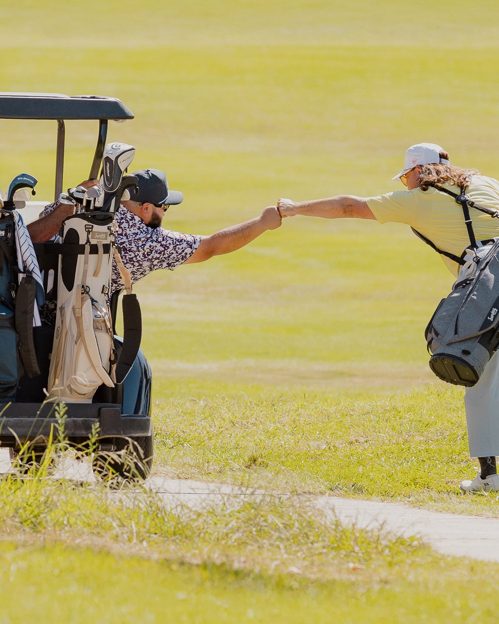 Two golfers bumping fists between a golf cart and a Sunday Golf stand bag