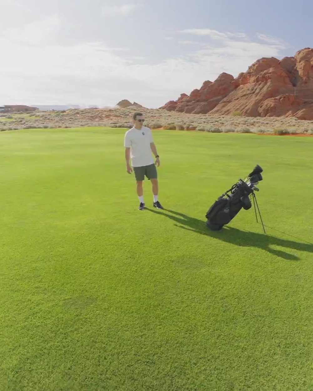A golfer walking a desert fairway beneath red rock cliffs with a Sunday Golf stand bag behind him