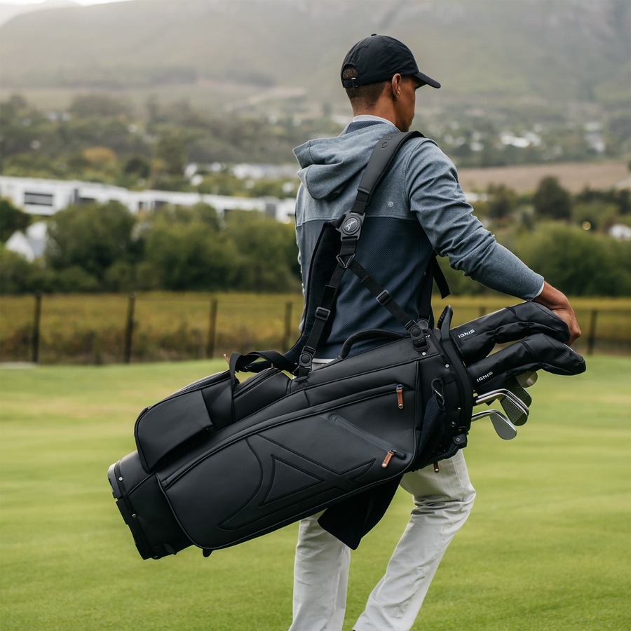 A golfer in a cap and hooded top walking a fairway with the black Stand Bag 02 on one shoulder