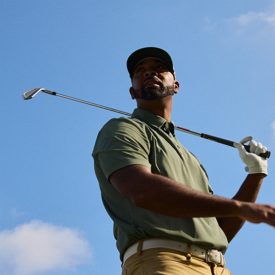 A golfer at the top of the backswing, shot from below against open sky