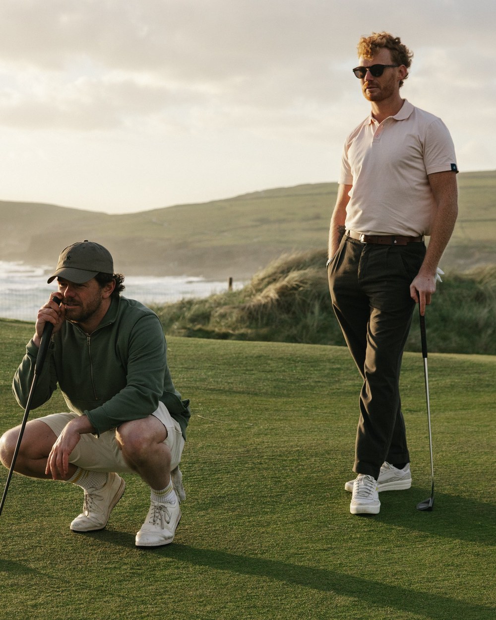 Two golfers in Sounder on a clifftop links green above the sea in Cornwall