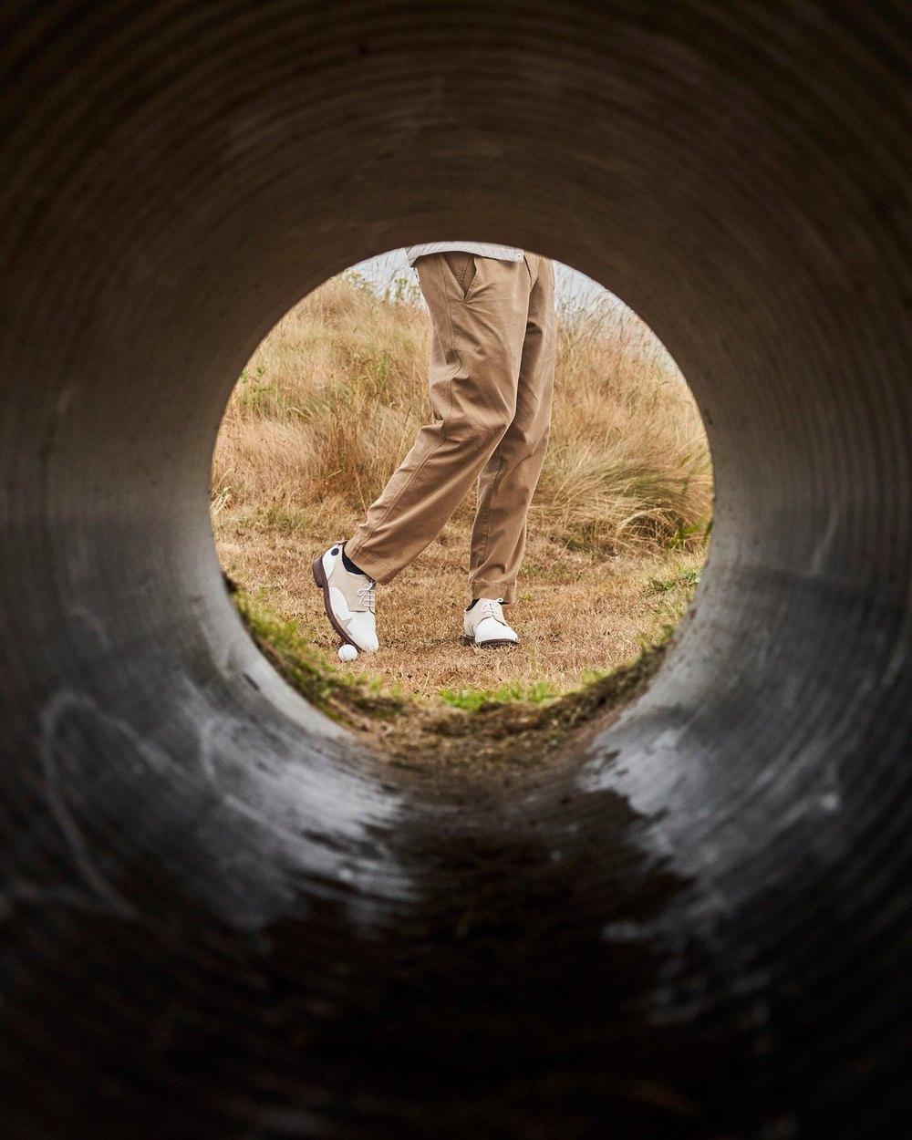 A golfer in Sounder trousers seen through a drainage tunnel on a links course