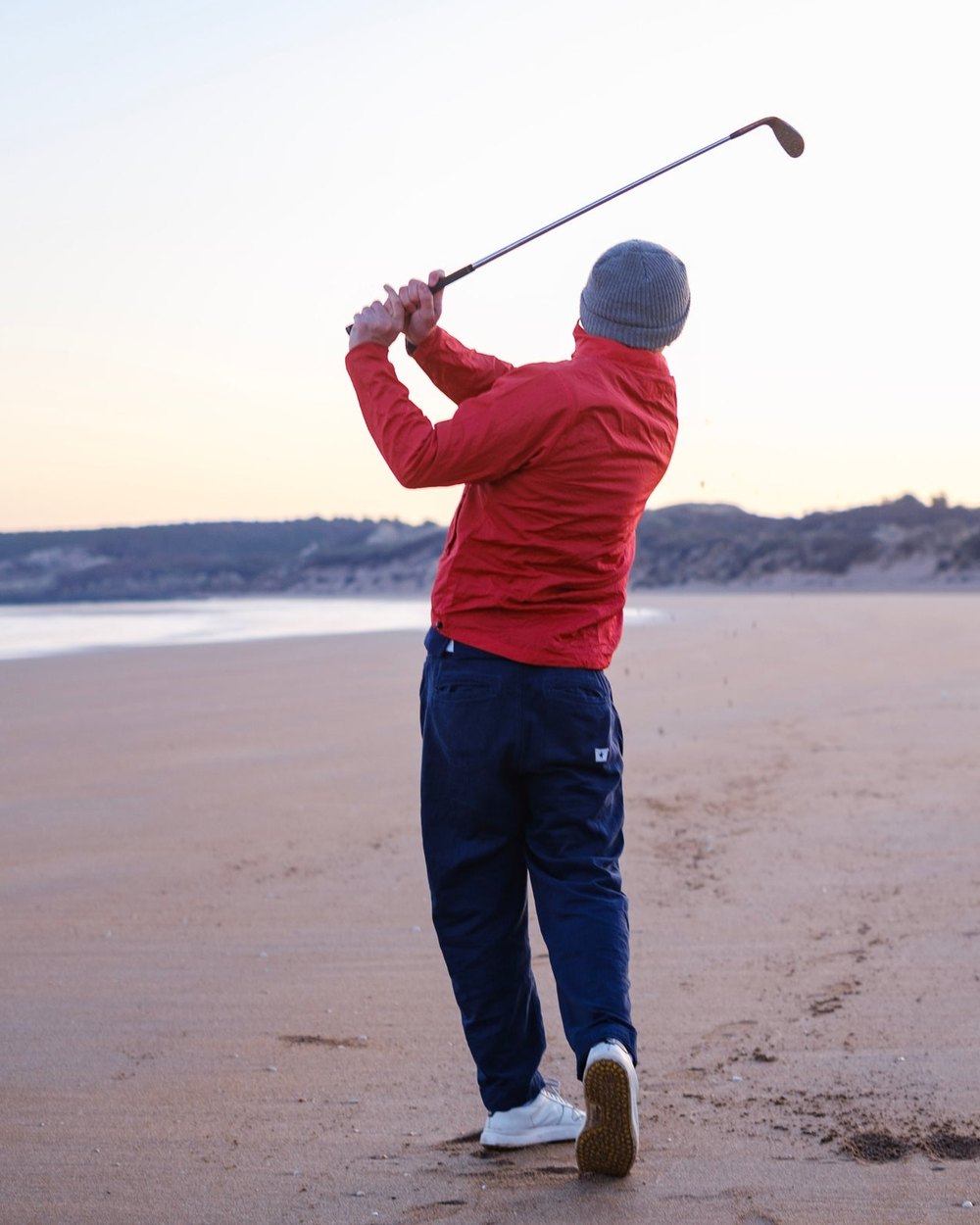 A golfer in a red Sounder Pac Mach jacket swinging on a beach