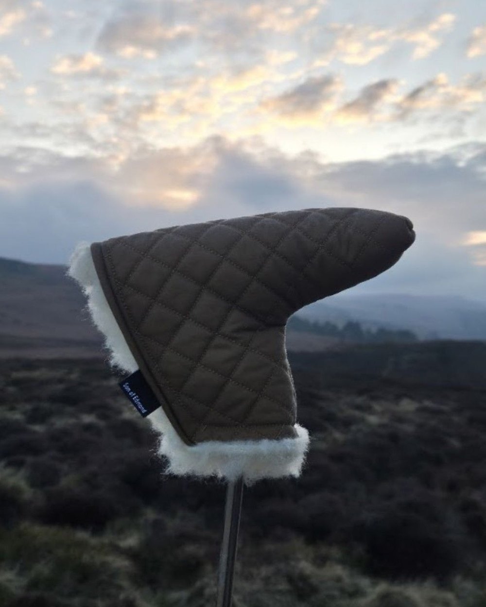 A quilted Son of Edmond putter cover against a moorland sky at dusk
