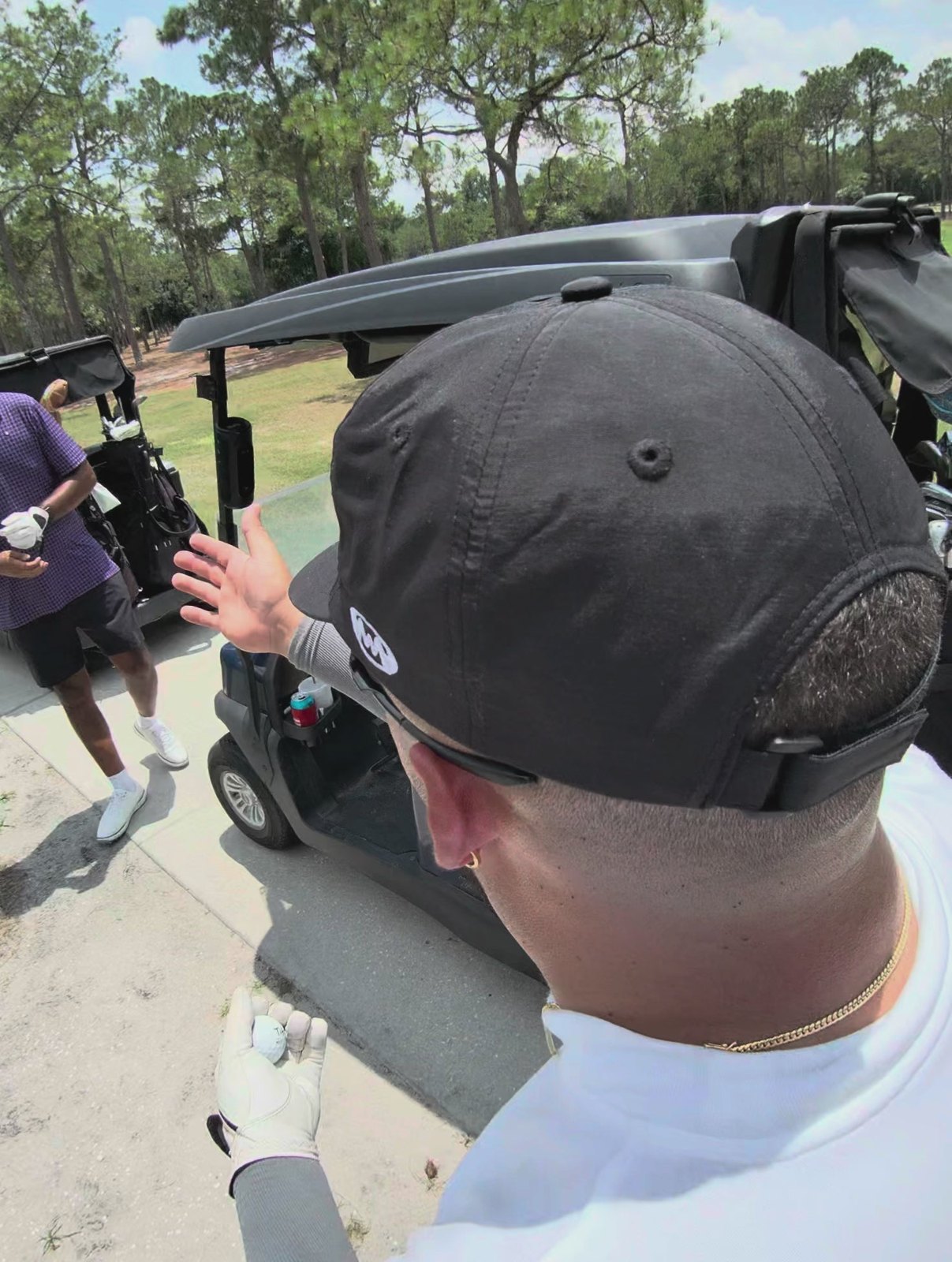 Looking over a golfer’s shoulder in a black Utility Cap toward a golf cart