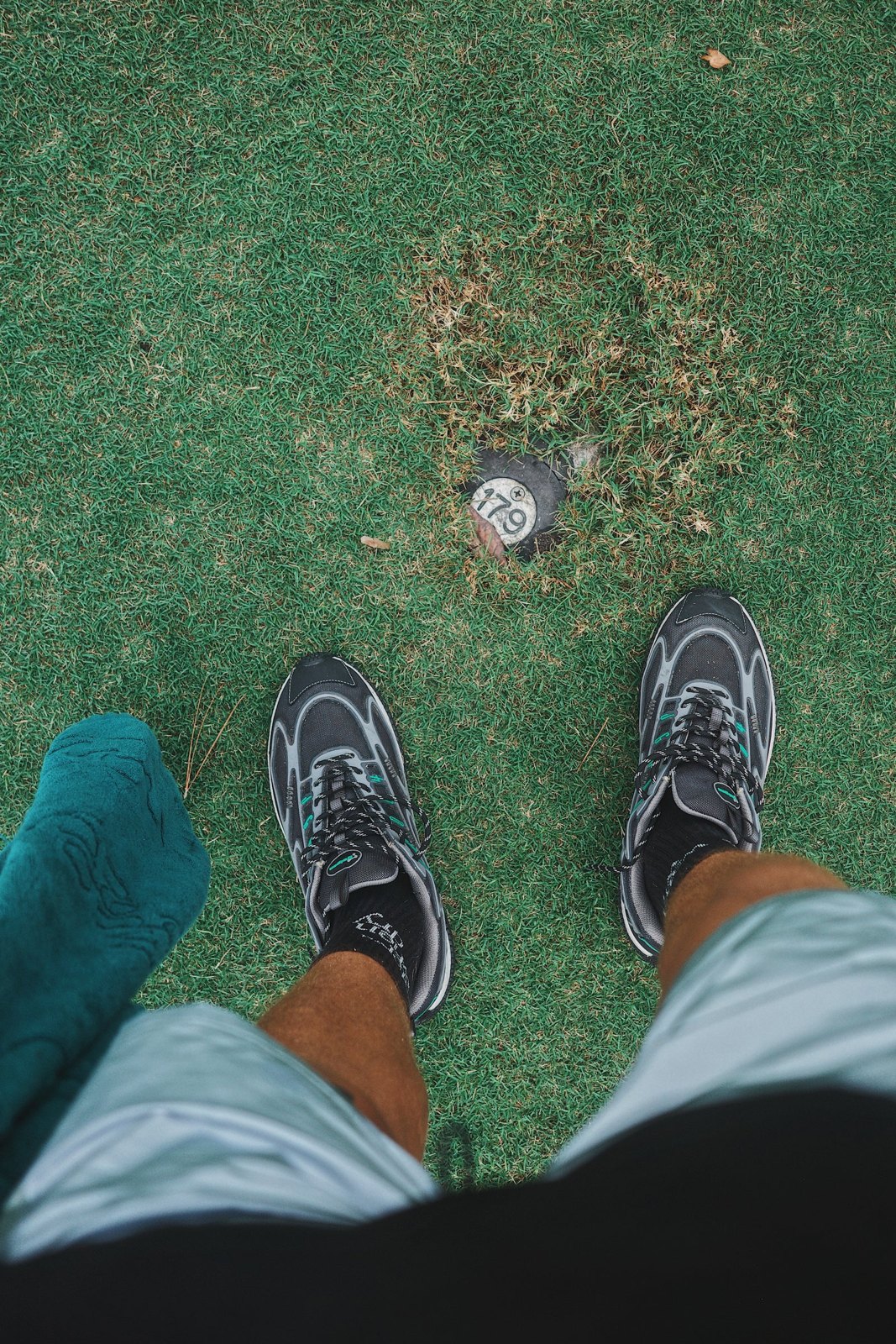 Looking down at grey running shoes and shorts on a putting green next to the hole