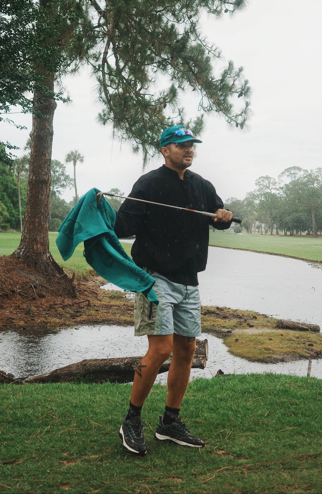 A golfer in a teal cap and the Camper Short waving a towel on a club by a pond