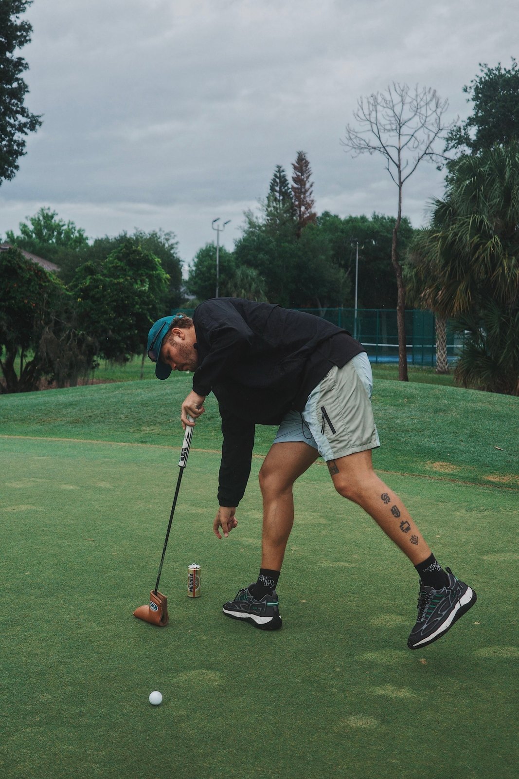 A golfer in the Camper Short bending to tee up a ball under palm trees
