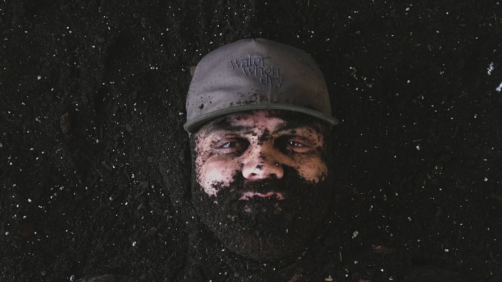 A man in a cap buried to his face in soil, from the brand’s About page