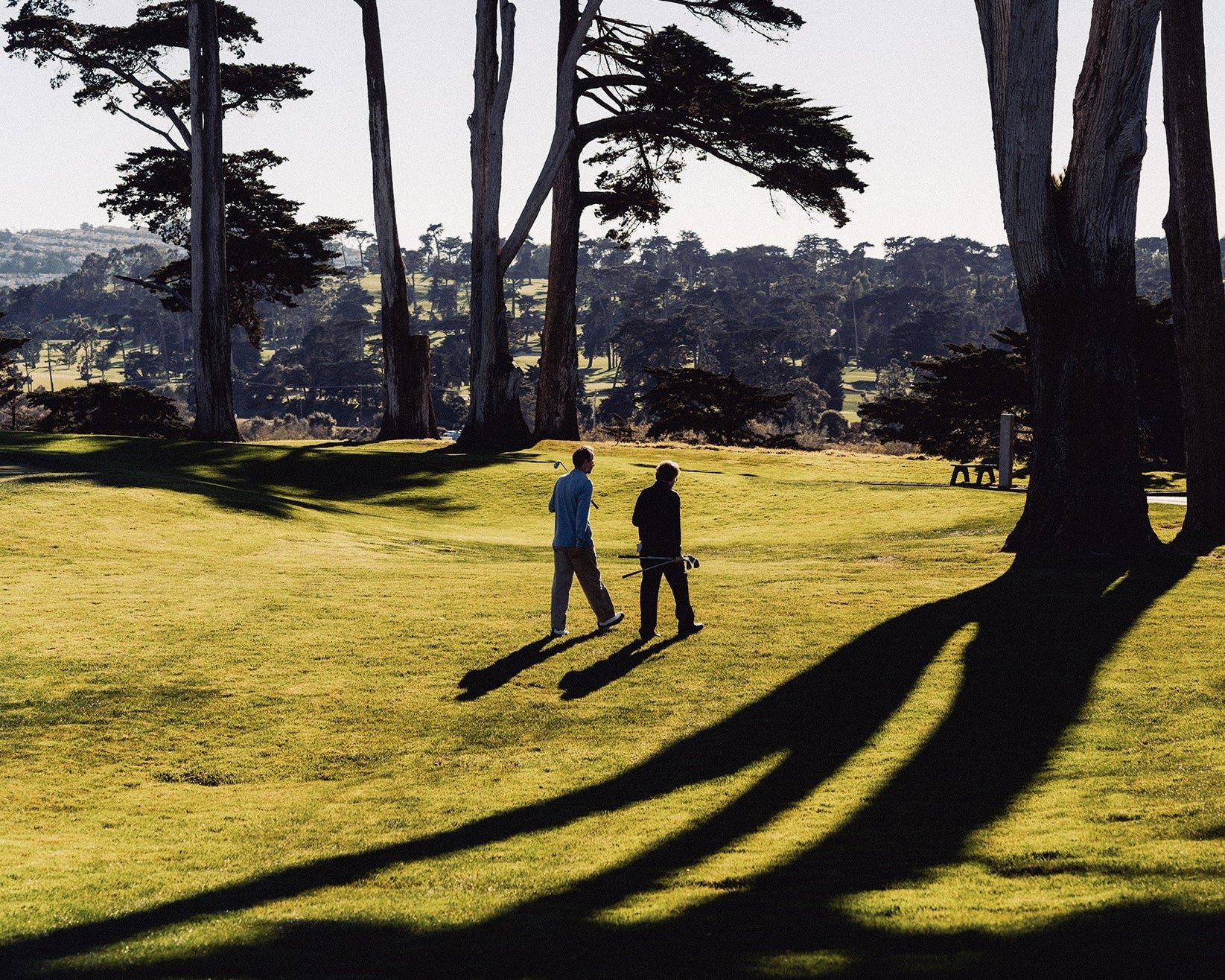 Two golfers walking under cypress trees on Whim's American merino trip in California