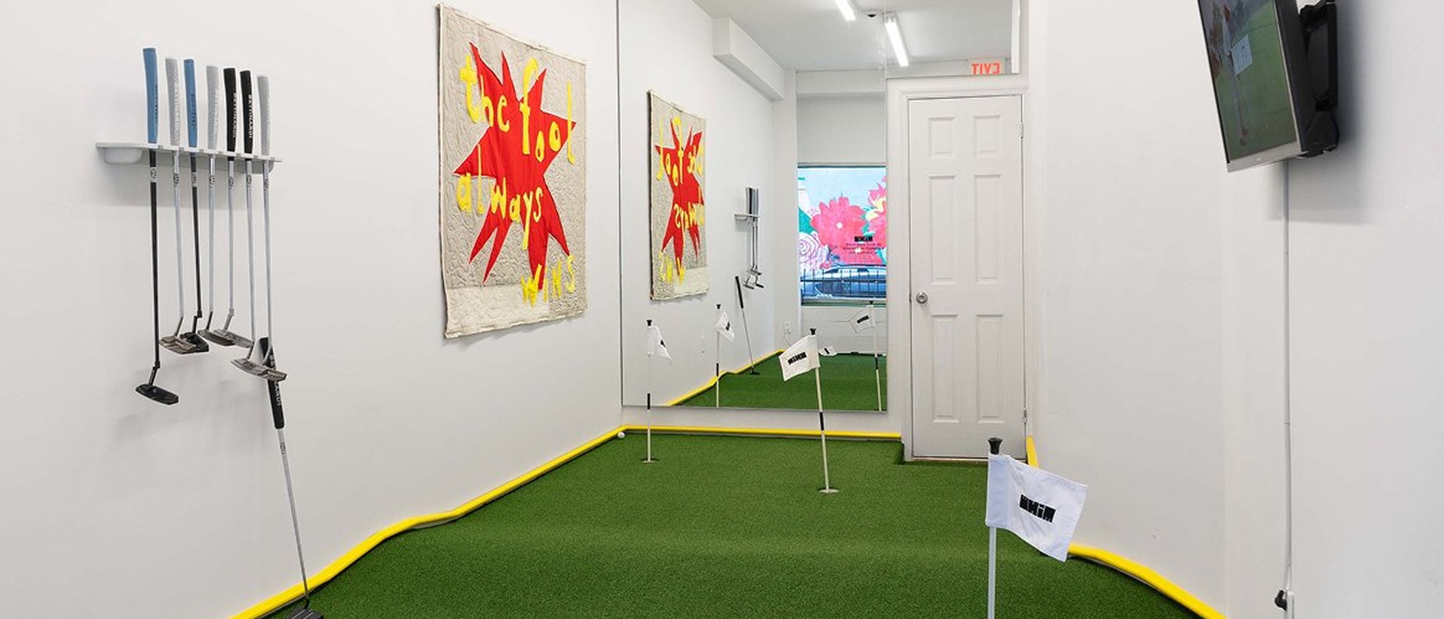 Whim Golf's free putting green at 129 Eldridge Street, New York, with putters on the wall and quilted artwork