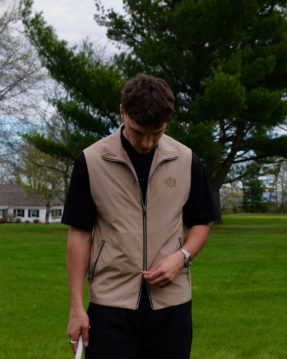 A golfer in the tan Woodgrain nylon vest on a fairway lined with pine trees